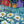 Load image into Gallery viewer, Daisies by Adam Young, white daisies and blue wildflowers before a picket fence and red, mustard and purple saltbox homes under a stormy teal sky

